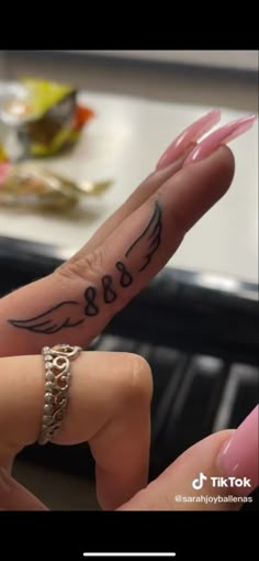 two fingers with tattoos on them and one has an angel wing tattooed on the middle finger