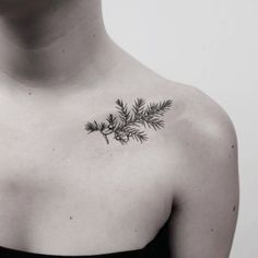 a black and white photo of a woman's shoulder with a pine branch tattoo on it