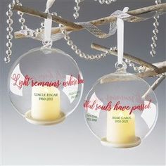 two clear glass ornaments hanging from a tree branch with a candle in each ornament