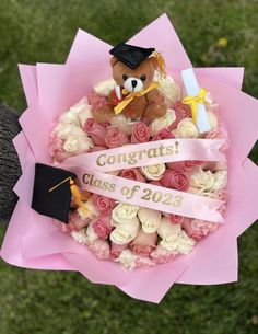 a teddy bear sitting on top of a bouquet of flowers with congratulations ribbon around it