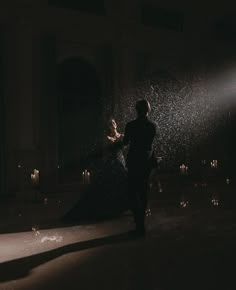 a man and woman standing in the dark with their arms around each other, surrounded by candles