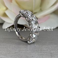 an image of a wedding ring with three stones on it and flowers in the background