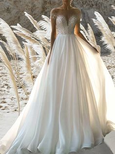 a woman in a white wedding dress standing on the beach with pamodia grass behind her