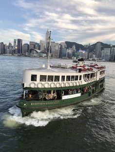 a green and white boat traveling on the water in front of a cityscape