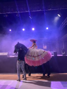 a man standing next to a woman on top of a horse in front of a stage