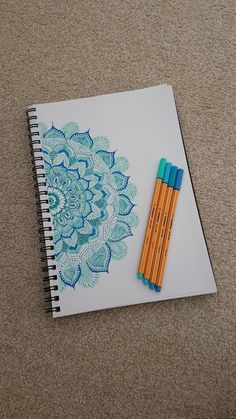 two pencils sitting on top of a spiral notebook with an intricate blue flower design