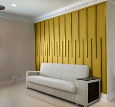 a white couch sitting in front of a yellow wall with vertical lines on the walls