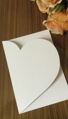 a white heart shaped card sitting on top of a wooden table next to a bouquet of flowers