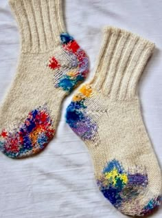 two pairs of socks with colorful paint splatters on them sitting on a white sheet