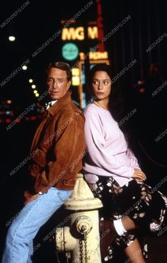 two people sitting on top of a fire hydrant in front of a neon sign