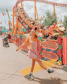 a girl is running in front of an amusement park roller coaster with characters on it