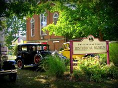 an old car is parked in front of the historical museum sign and flowers on display