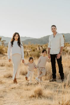 a man and woman holding hands while walking with two small children in the middle of an open field