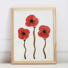 three red flowers in a wooden frame on a white table next to a wall and floor