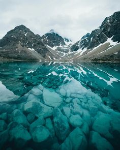 the mountains are reflected in the water and ice on the rocks near the lake's edge