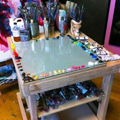 a table with lots of paint and brushes on it, in the middle of a room