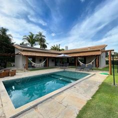 an empty swimming pool in front of a house with hammocks hanging from the roof