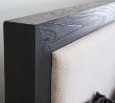 an upholstered headboard on a bed with black wood and white linens