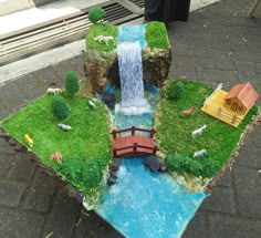 a miniature waterfall and bridge made out of fake grass with animals in the pond below