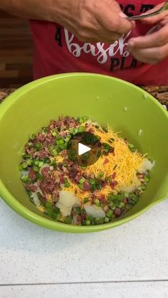 a bowl filled with vegetables and cheese on top of a counter next to a person holding a cell phone