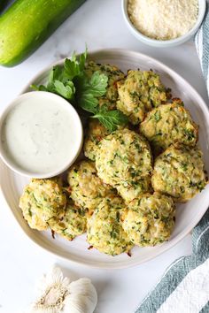 a white plate topped with crab cakes next to a bowl of sauce and a cucumber