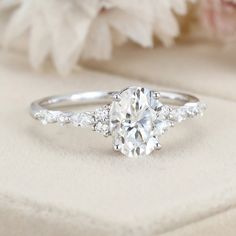 an oval cut diamond ring with three side stones on the band and a flower in the background