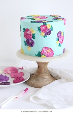 a blue cake with pink and yellow flowers on it sitting on top of a wooden stand