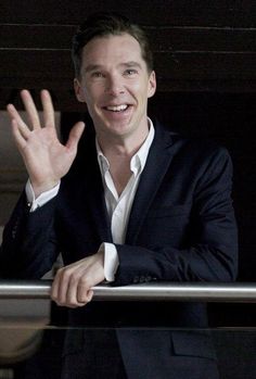 a man in a black suit and white shirt waving