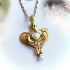 "Found is this beautiful gold and pearl lavalier pendant from the Art Nouveau (ca 1910) era. This delicate piece is made of vibrant, brushed 14k yellow gold and has a flowing stylized heart shape approx. 32 mm long x 21 mm wide x ⅛\" thick. The pendant has a leaf motif with delicate, leaf-like swirls adorned with soft enameling in hues of green and yellow. In the center of the pendant is a single freshwater pearl.  Dangling freely from the base of the pendant is another l4.2 mm x 5mm  pearl. The Elegant Heart Pendant Necklace For Collectors, Art Deco Pearl Pendant Jewelry, Art Nouveau Yellow Gold Jewelry Gift, Victorian Yellow Gold Heart Pendant Necklace, Gold Art Deco Necklace With Pearl Pendant, Art Nouveau Yellow Gold Pendant Jewelry, Art Nouveau Yellow Gold Necklace For Formal Occasions, Art Nouveau Yellow Gold Formal Necklace, Collectible Art Nouveau Yellow Gold Jewelry