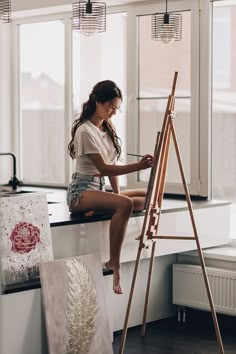 a young woman sitting on top of a counter next to an easel and painting