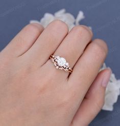 a woman's hand with a diamond ring on her left hand and white flowers in the background