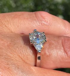 a close up of a person's hand holding a ring with an oval shaped diamond