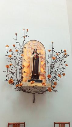 a statue of the virgin mary surrounded by flowers and branches in front of a white wall