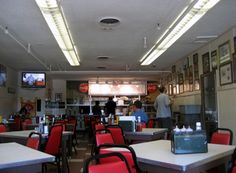 the inside of a fast food restaurant with red chairs and white tables, people are standing in the background