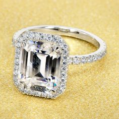 an emerald cut diamond ring with pave diamonds surrounding it on a gold glitter background