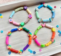 four colorful bracelets on a tray with buttons and beads in the shape of flowers