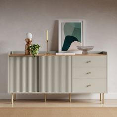 a sideboard with three drawers and plates on it in front of a wall mounted art piece