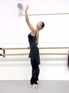 a woman in black dress standing next to a ballet pole with her arm raised up