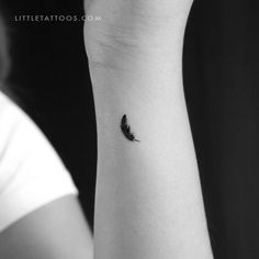 a small black feather tattoo on the left inner arm, with a woman's hand holding