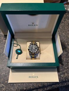 This Rolex Submariner wristwatch features a unidirectional rotating black bezel on a silver and gold oyster bracelet. The 40 mm stainless steel case houses a mechanical (automatic) movement with 31 jewels, including a date indicator, chronometer, and self-winding function. The watch is water-resistant up to 300 m (30 ATM) and comes with original box/packaging, manual/booklet, and papers. The watch has a deployant closure and a lug width of 20 mm, with a maximum wrist size of 7.6-8 inches. The black dial features arrow, baton, and round indexes, as well as sapphire crystal and a solid caseback. This Swiss-made watch is a great addition to any collection and is sure to impress. Rolex Submariner Black Gold, Vintage Omega Watches, Rolex Submariner Black, Rolex Watches Submariner, Submariner Watch, Omega Watch Vintage, Rolex Watches Women, Rolex Watches For Men, Men's Watches Luxury