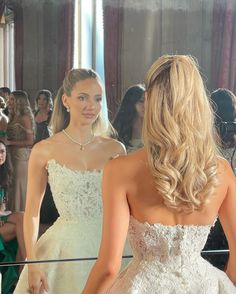 a woman in a wedding dress looking at herself in the mirror with another woman standing behind her