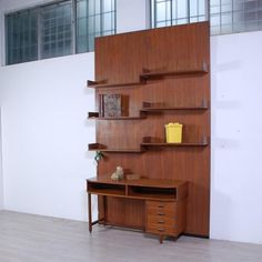 a wooden desk sitting in front of a wall with shelves on top of it and a yellow vase next to it