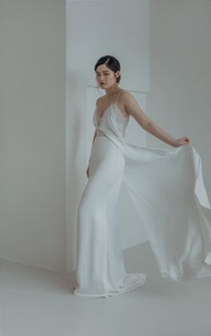 a woman in a white dress is standing by a wall with her arms spread out