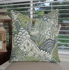 a green and white pillow sitting on top of a chair next to a window covered in blinds