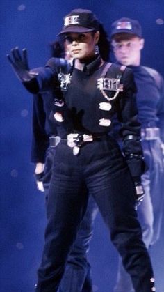 a woman in black outfit standing on stage with two other people behind her and one person wearing