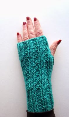 a woman's hand wearing a green knitted fingerless mitt on top of a white wall