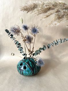 a vase filled with flowers and plants sitting on top of a white table covered in dry grass