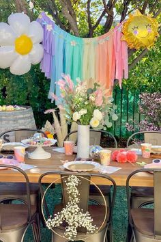 an outdoor table set up for a party with balloons and flowers in the background,