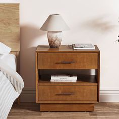 a nightstand with two drawers and a lamp next to it on a wooden floor near a bed