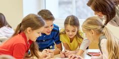 a group of children sitting around a table with their hands on the paper and writing